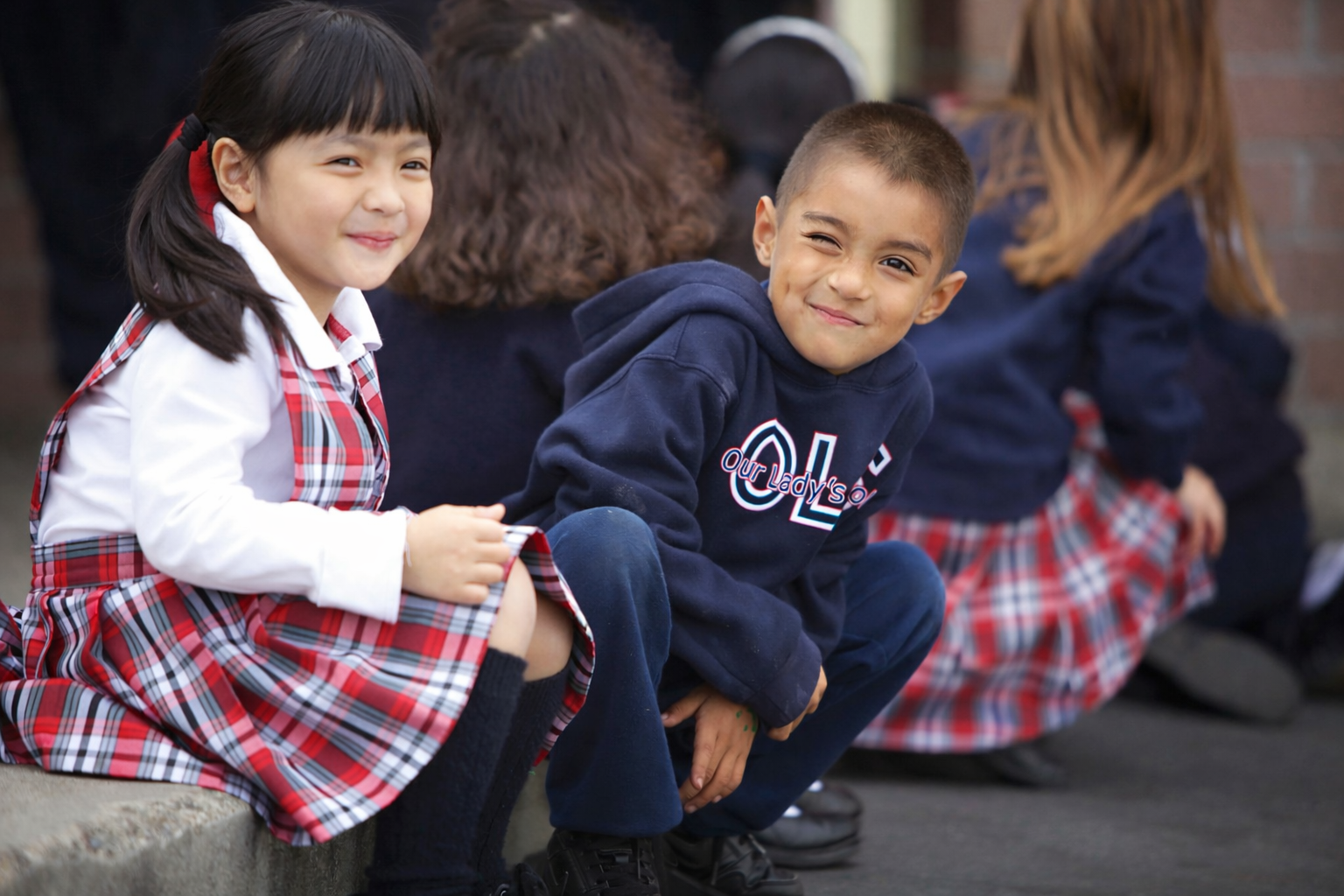 Students in school uniforms outside on campus grounds smiling.