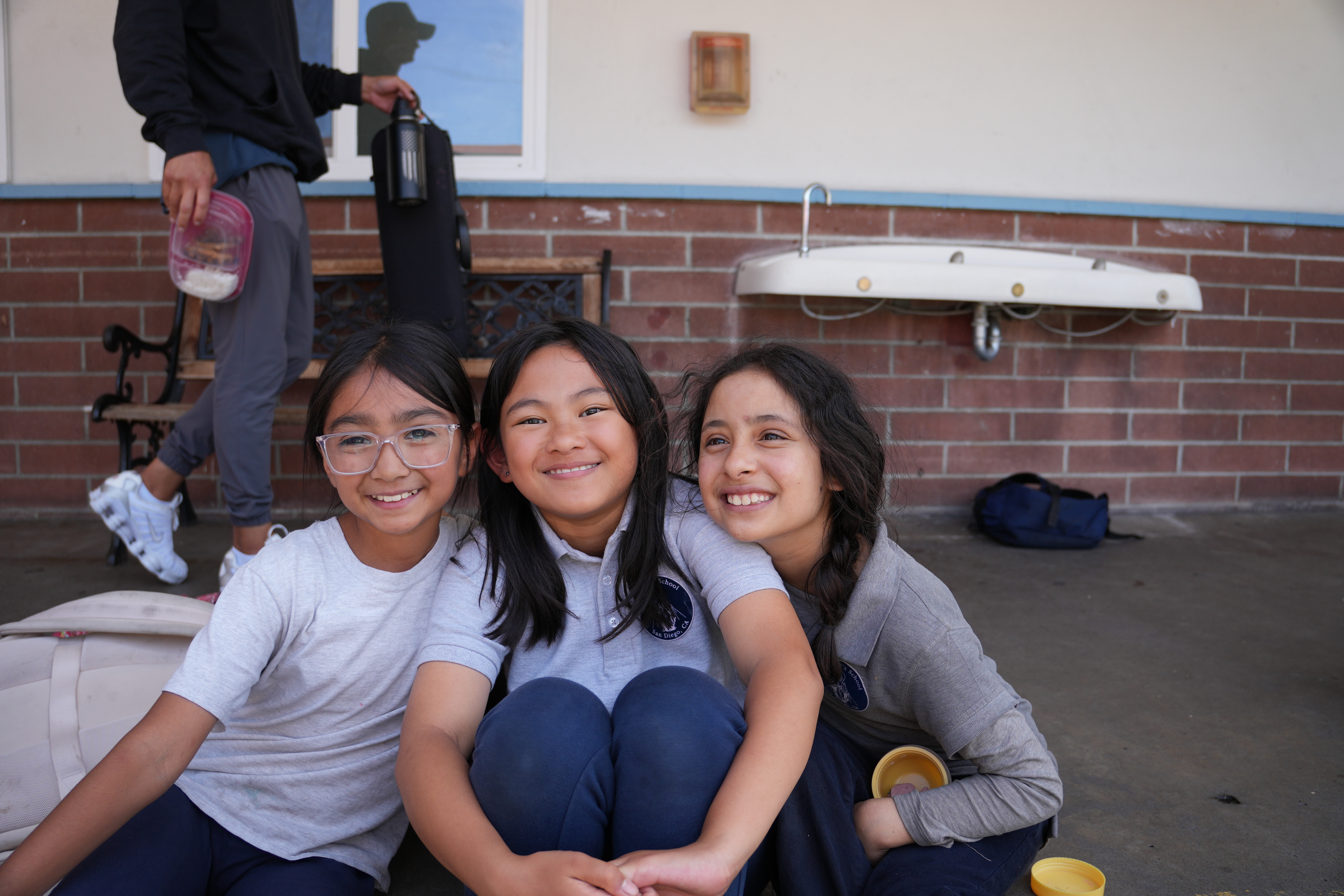 Three students smiling and sitting together on school grounds demonstrating the welcoming community at Our Lady's School.