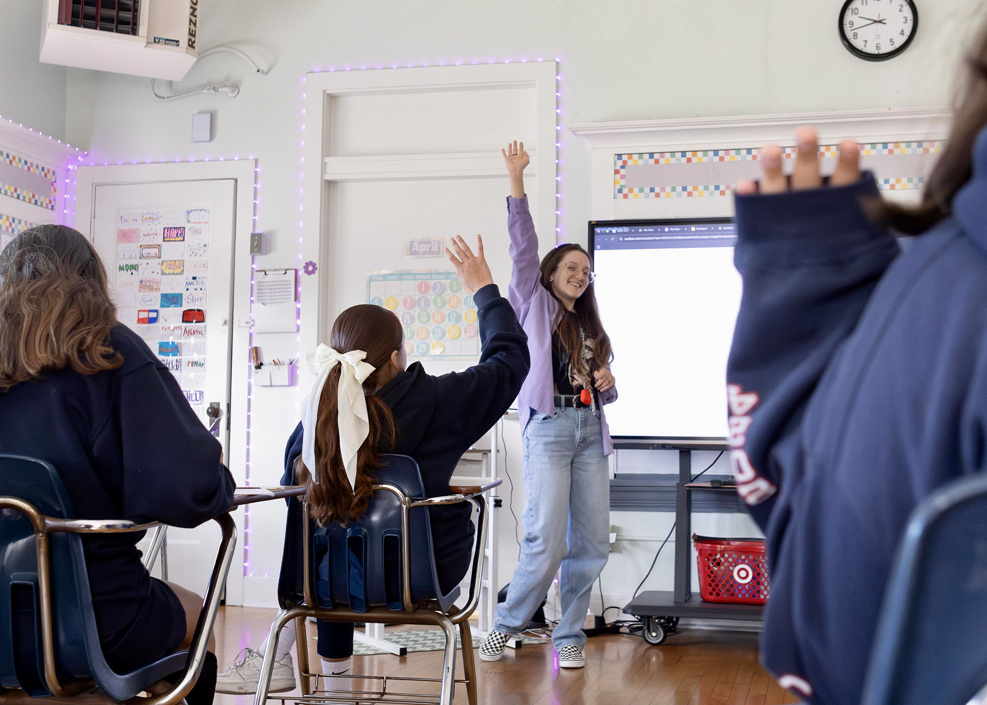 Students raising hands to a teacher giving a presentation.