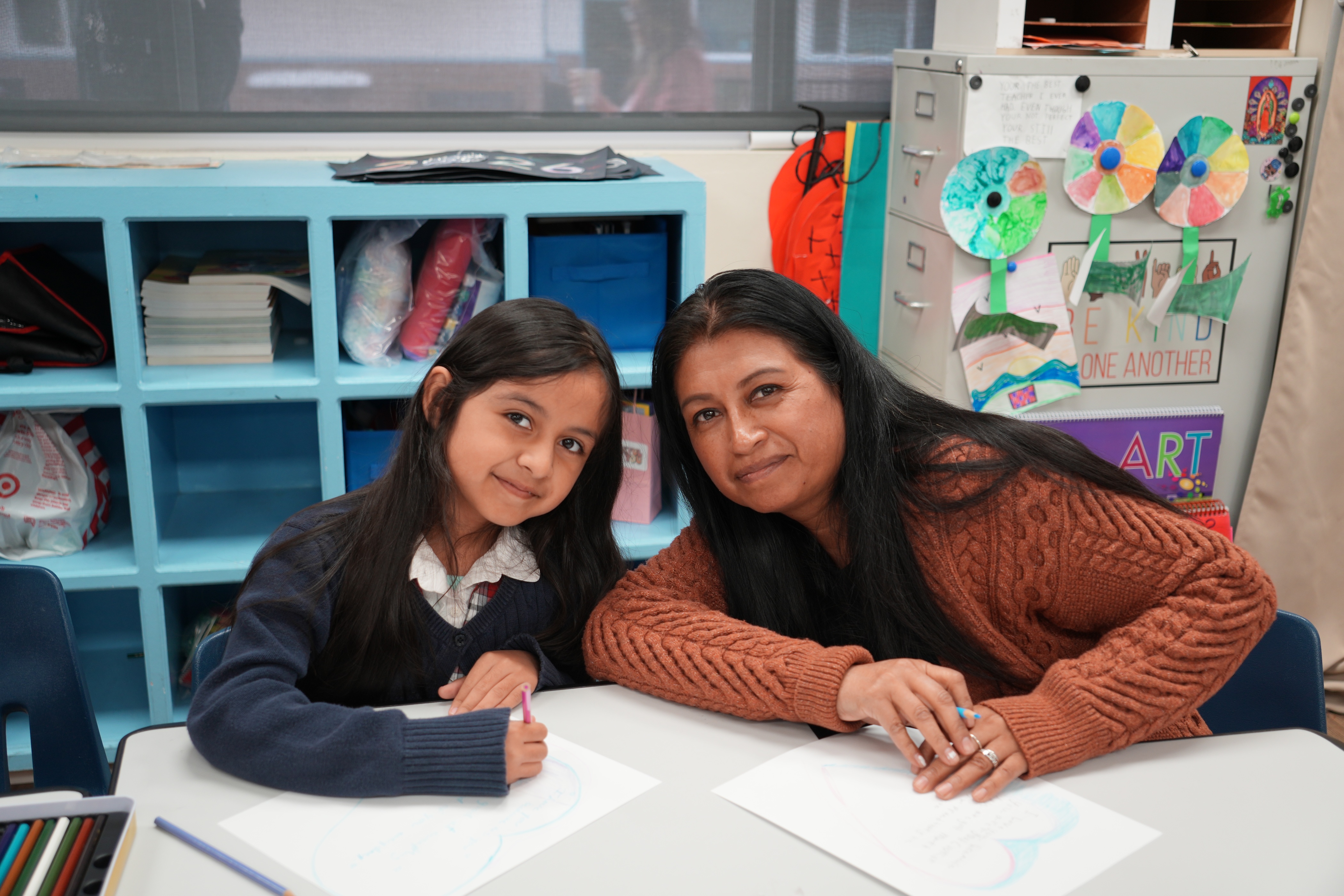 Teacher and student working together at a desk with art supplies, demonstrating supportive classroom learning environment.